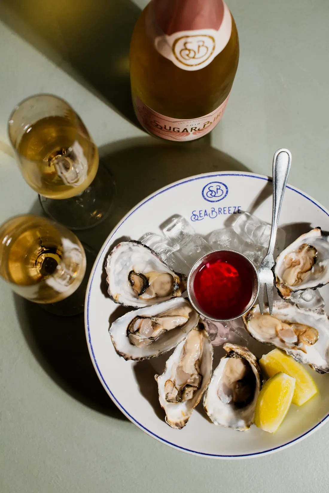 Natural oysters on ice on a SeaBreeze plate with lemon, mignonette and a bottle of SugarBird Cap Classique